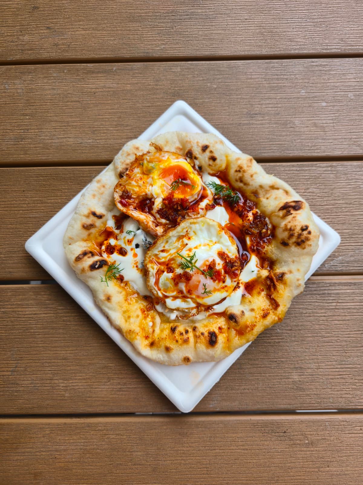 A Turkish Egg Fritta plated — egg, yoghurt and spiced toppings on pan-fried dough