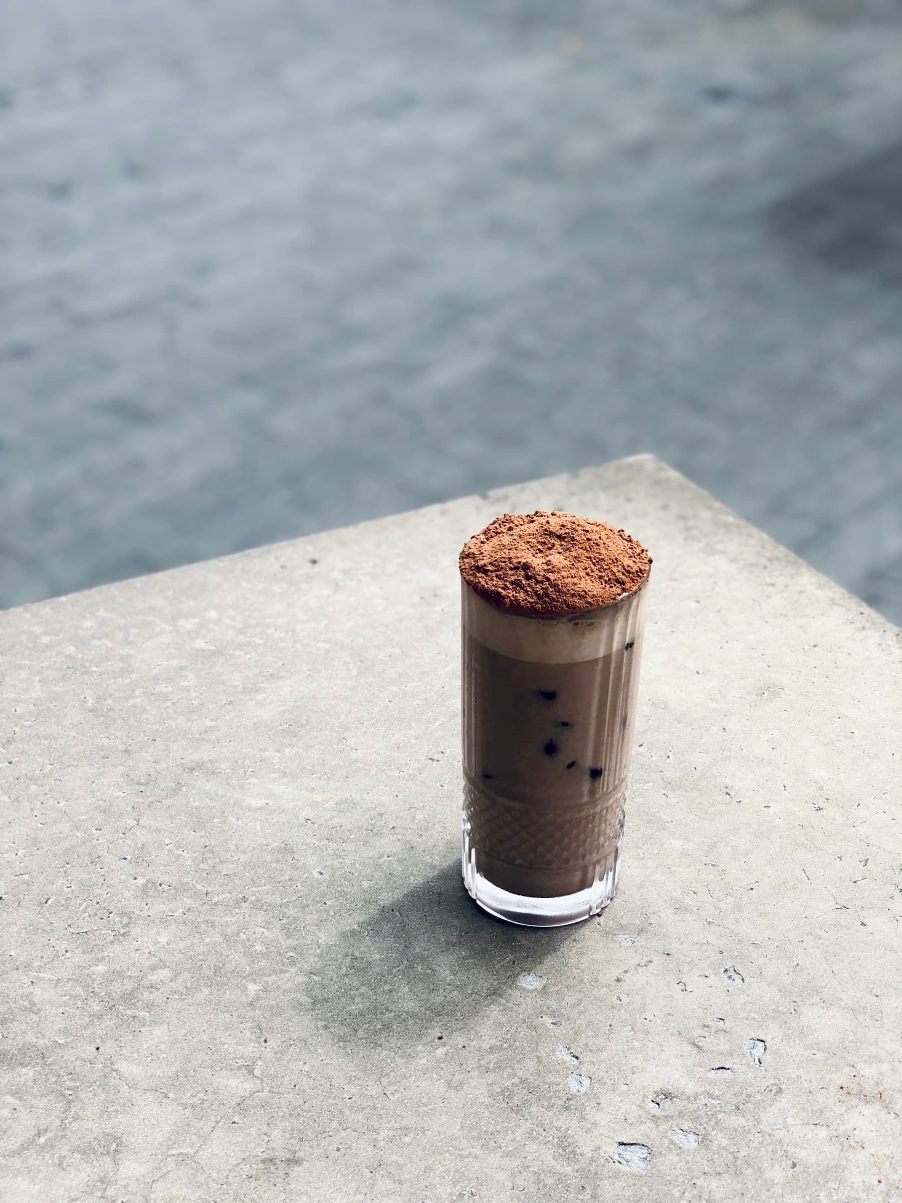 Iced mocha topped with cocoa powder, on the polished concrete bench by the harbour