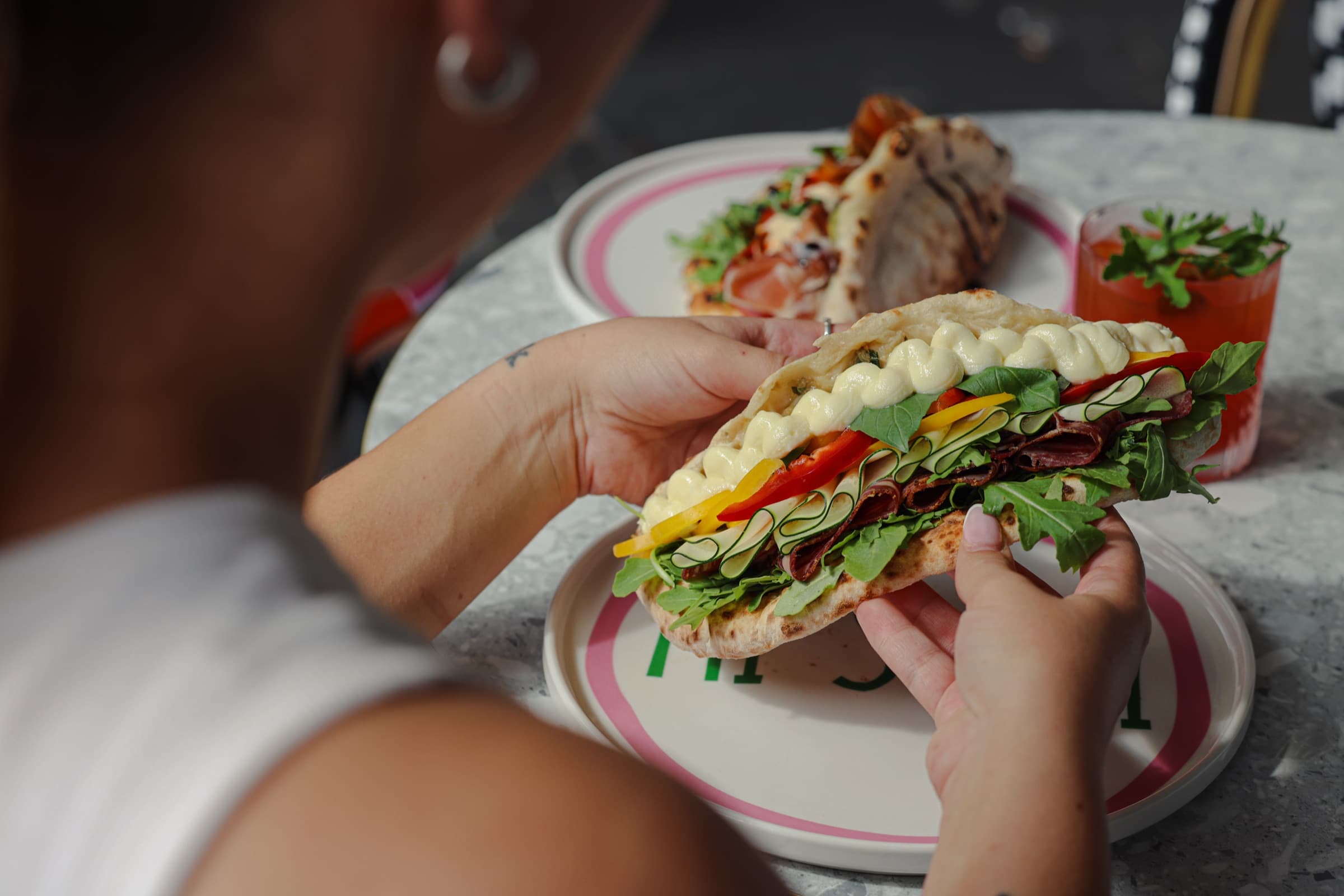 An open ozzo on a pink-rimmed plate — arugula, capsicum, prosciutto, citrus stracciatella