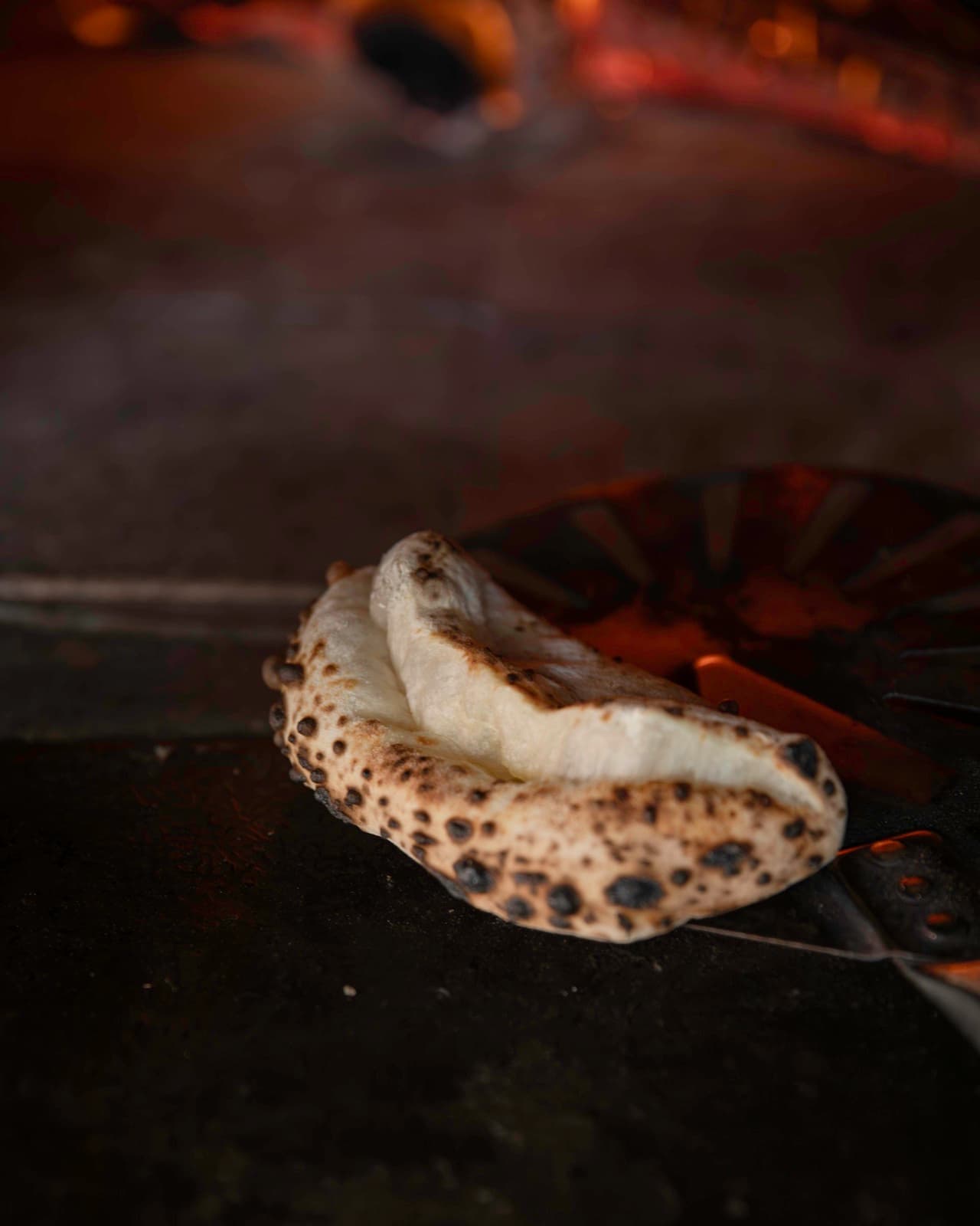 A finished Ozzo fresh from the wood oven, its surface blistered with dark leopard-spotting from the fire
